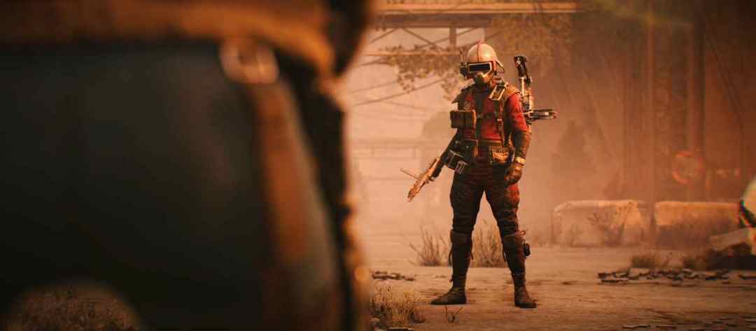 A Raider in a red suit and visor helmet stands in a dusty street with a rifle, seen past the shoulder of another Raider